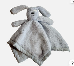 A plush blue dog comforter featuring a stuffed dog head with floppy ears and a flat, square blanket body made of soft, fuzzy light-blue fabric with a fabric border.