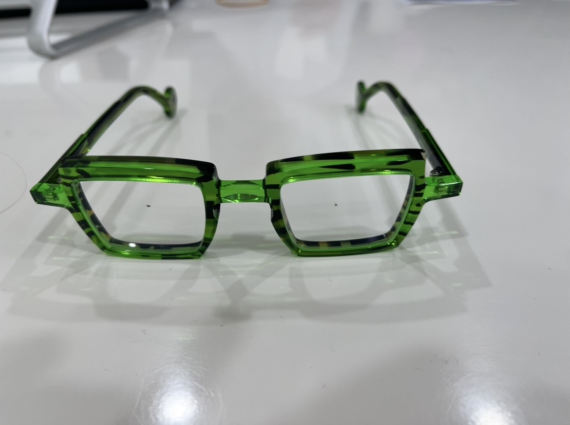 pair of prescription reading glasses featuring thick, bold, square-shaped frames. The frames are made of translucent, bright green material with dark tortoiseshell-style mottled patterns, resting on a plain white surface.